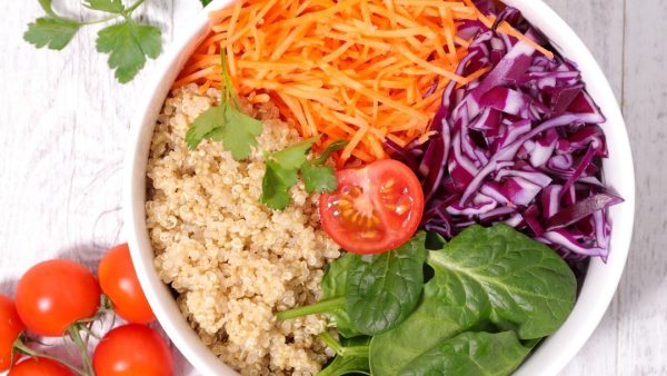 a bowl of food with quinoa, shredded carrots, cabbage and spinach