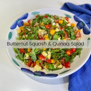 A salad platter filled with salad that includes butternut squash, tomatoes, quinoa, arugula and cheese cubes.
