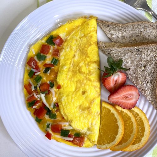Cheese and veggie omelette on a white plate served with orange slices, strawberries and toast