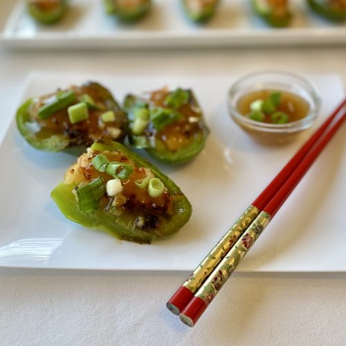 Dim sum stuffed green peppers on a white platter with red chopsticks and a small bowl of sauce