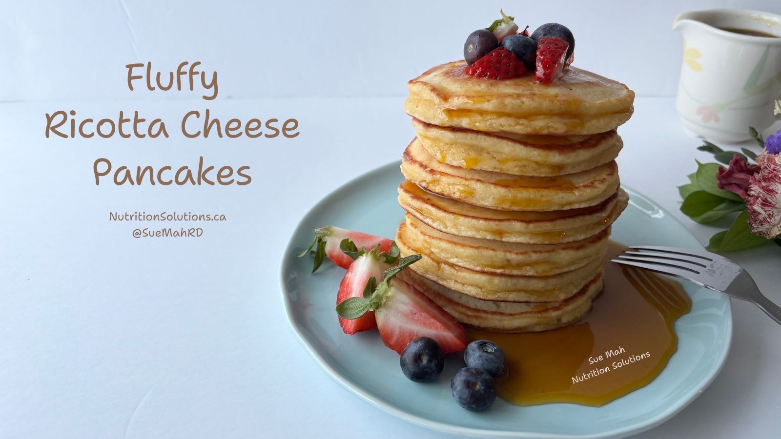A plate of stacked pancakes drizzled with maple syrup. Fresh blueberries and strawberries are on the plate.