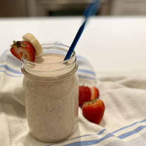 A cup of smoothie decorated with a slice of strawberry, banana and blue straw