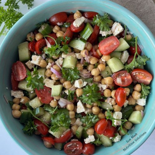 A bowl with chickpeas, feta cheese, tomatoes, cucumbers and parsley