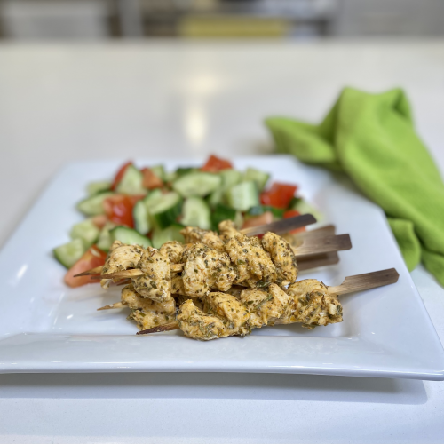 Chicken skewers and salad on a white plate, with a green napkin beside it