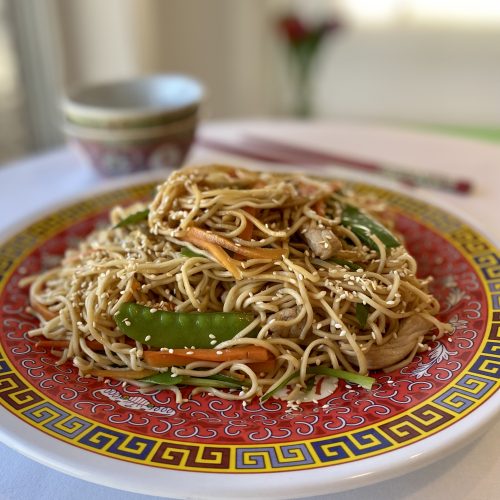 A meal of pork stir fry arranged on a beautiful Chinese red platter.