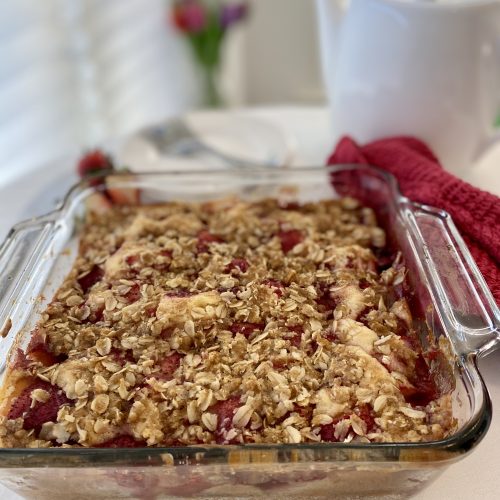 Strawberry cobbler cake in a glass baking dish, arranged beside a white teapot